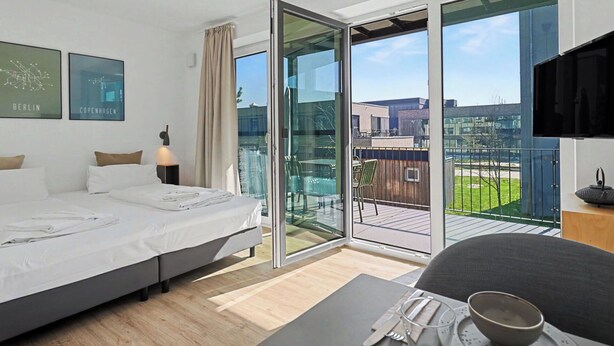 Una camera d'albergo moderna con un letto, un tavolo da pranzo con posate, una TV e un balcone con vista sulla città.