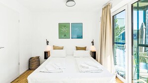 Un letto matrimoniale con lenzuola bianche, due lampade fissate al muro, un comodino e due quadri incorniciati raffiguranti Berlino e Copenaghen.