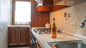 Une cuisine avec des meubles de rangement en bois, un évier en acier inoxydable, une bouteille d’huile d’olive et un verre à vin.