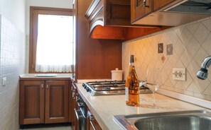 A kitchen with wooden cabinets, a stainless steel sink, a bottle of olive oil, and a wine glass. - Casa Lucia - Three Bedroom Apartment, Sleeps 5 (Posada)