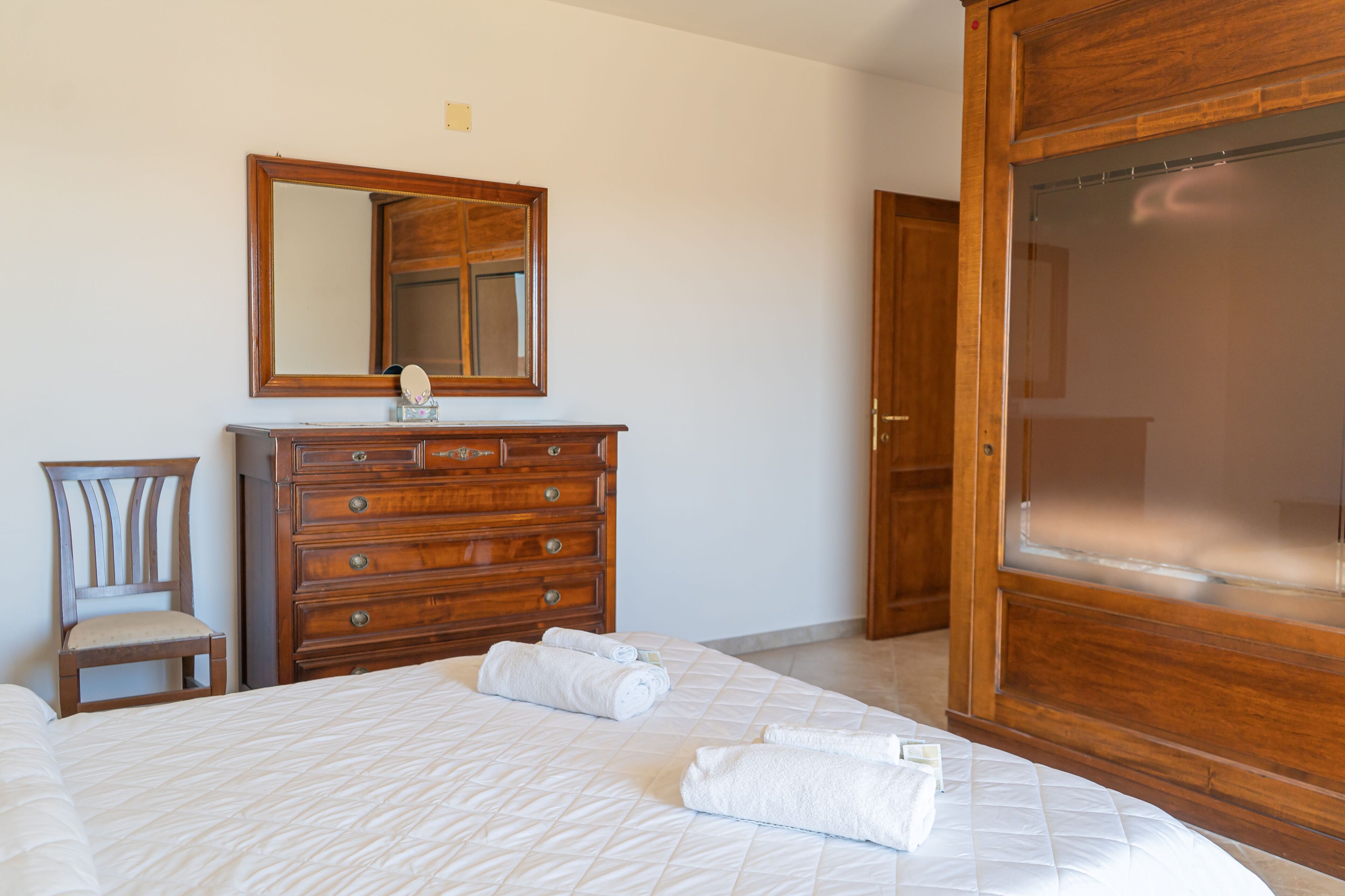 Une chambre à coucher comprenant un lit, une commode en bois, une chaise, un miroir et une armoire.