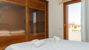 Une chambre à coucher avec un lit, une armoire en bois et une vue sur l’extérieur par une porte ouverte.