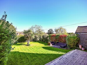 Un jardin bien entretenu, avec une pelouse, une terrasse en bois et divers arbustes et arbres.