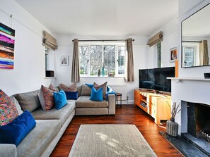 A living room with a sofa, television, fireplace, and large windows. - Beautiful  villa for 6 guests with WIFI (Lewes)