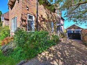 Une maison en briques avec un garage, entourée d’une végétation luxuriante et dotée d’une allée gravillonnée.