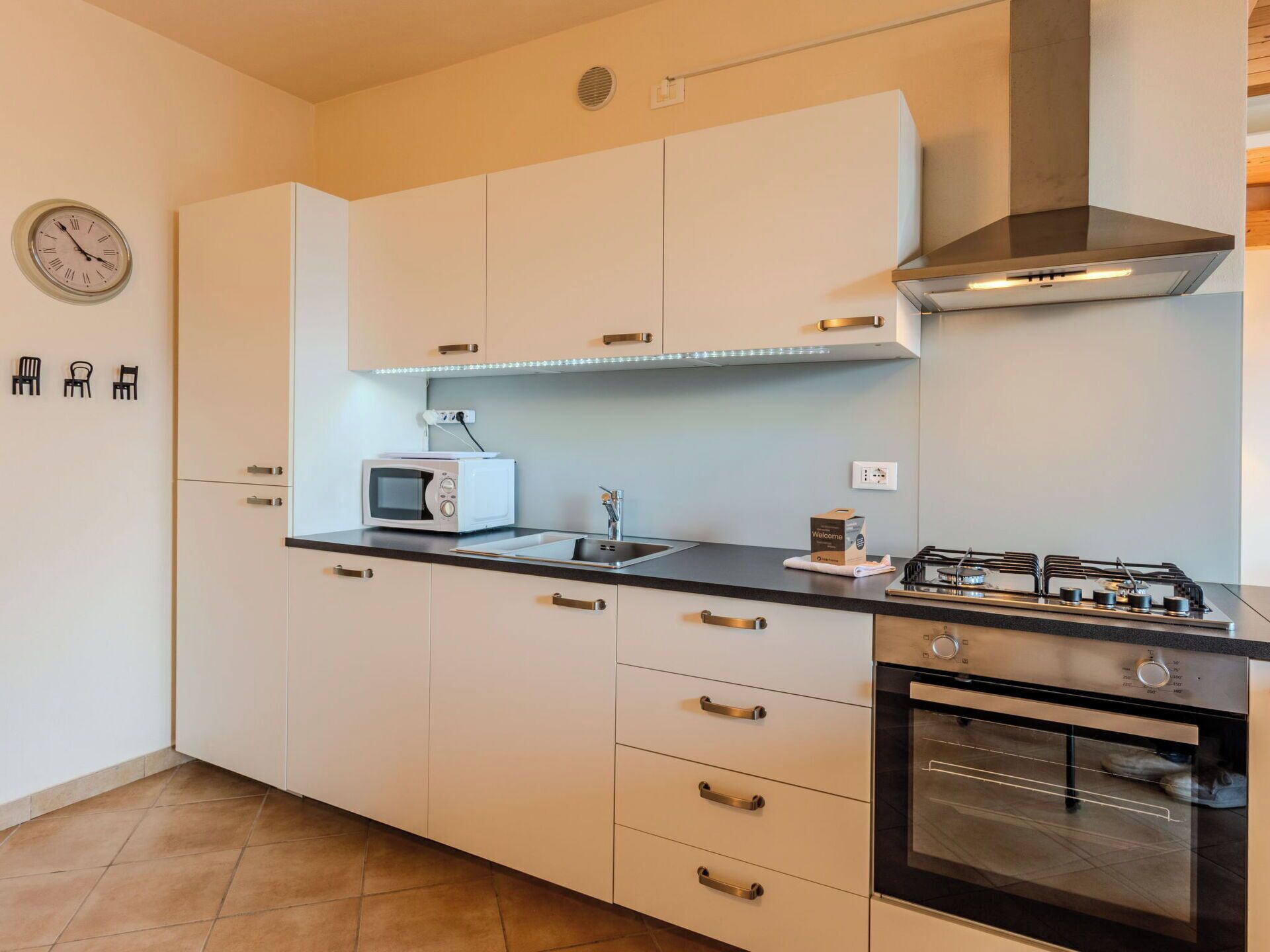 Une cuisine moderne avec des meubles blancs, un four à micro-ondes, une cuisinière à gaz et un four encastré.