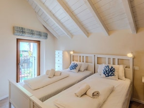 Ein Schlafzimmer mit zwei Betten, einer Holzbalkendecke, einem Fenster mit Blick und einer Tür.