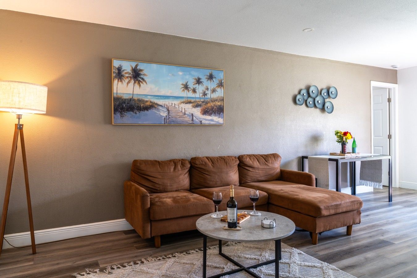 Spacious Open-Concept Living Room: Unwind in luxury on this plush brown sectional sofa, framed by a stylish tripod floor lamp, coastal-inspired wall art, and an open layout that connects seamlessly to the dining space.