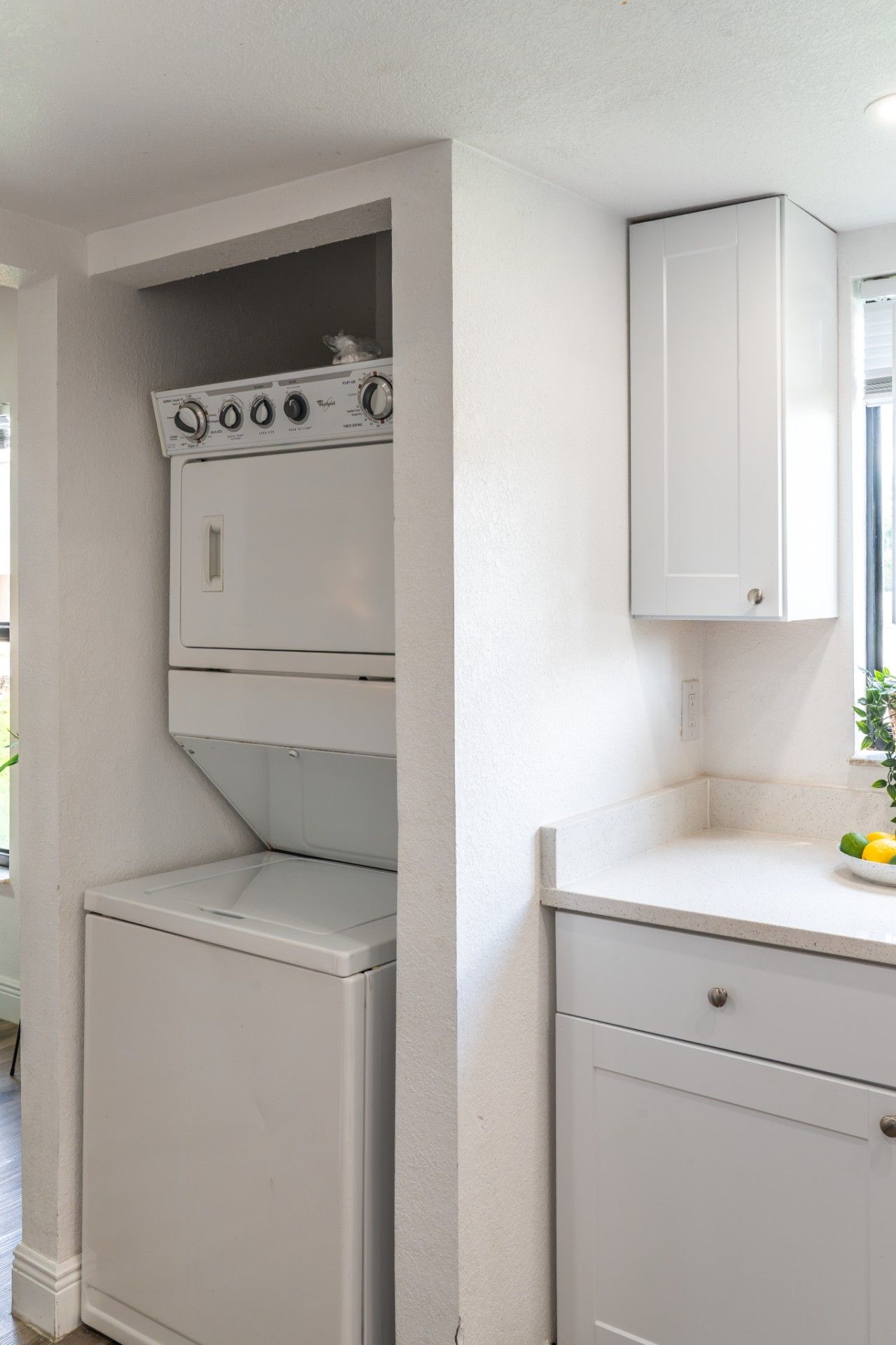 In-Unit Laundry & Storage Nook: Enjoy total travel convenience with a stacked in-unit washer and dryer tucked off the hallway, clean white cabinetry storage, and bright natural lighting from the adjacent window.