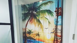 Een badkamer met een douchegordijn waarop een tropisch strand afgebeeld is.