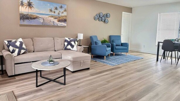 Een woonkamer met een bank, een voetenbankje, een salontafel en blauwe fauteuils.