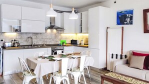 Cocina moderna con armarios blancos, comedor con sillas blancas y sala de estar con sofá y mesa de centro.