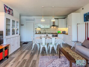 Cozinha moderna com armários brancos, uma mesa de jantar posta para quatro pessoas e um sofá na sala de estar.