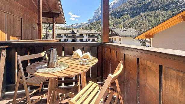 Ein Holzbalkon mit Tisch und Stühlen, mit Blick auf ein Bergdorf mit traditioneller Bebauung.