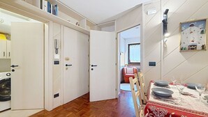 Ein Essbereich mit Tisch für zwei Personen, Holzboden und Blick in ein Wohnzimmer mit einem roten Sessel.