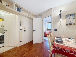 Ein Essbereich mit Tisch für zwei Personen, Holzboden und Blick in ein Wohnzimmer mit einem roten Sessel.