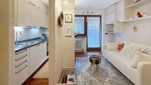 Ein kompakter Wohnbereich mit einer Küchenzeile, einem Sofa und einem kleinen Hocker.
