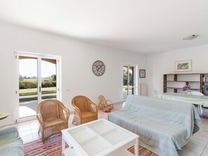 Ein Zimmer mit einem Bett, zwei Korbstühlen, einem Tisch mit einer Vase, einer Uhr und einem Bücherregal.