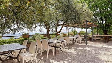 An outdoor patio with tables and chairs, surrounded by trees and overlooking a body of water.