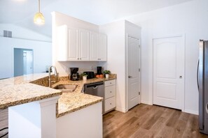 A modern kitchen with white cabinetry, a granite countertop, and a stainless steel refrigerator.