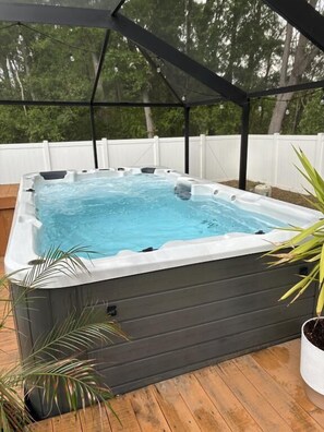 A hot tub with a wooden deck and a white fence in the background.