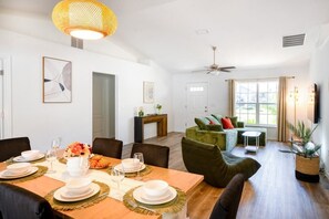 A dining area with a wooden table set for four, surrounded by chairs. There is a sofa and a small table in the background.