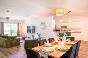 A modern living room with a dining area, a kitchen, and a ceiling fan.