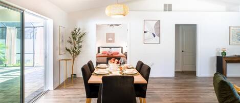 A dining area with a wooden table set for four, surrounded by black chairs, a hanging light fixture, and framed artwork on the walls.