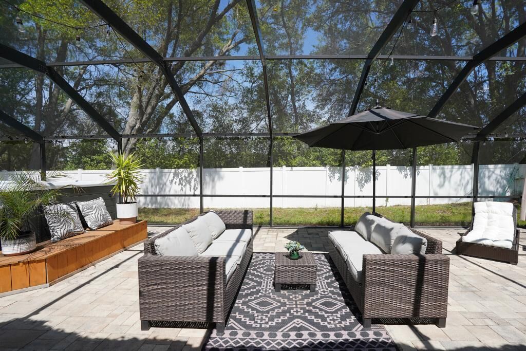 Eine Terrassengruppe im Freien mit Korbmöbeln, einem gemusterten Teppich und einem großen Sonnenschirm.