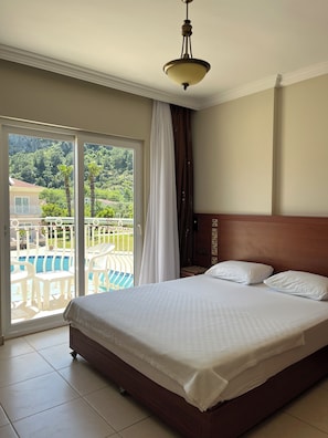 Habitación de hotel con cama, vista a una piscina y balcón con vistas a las montañas.