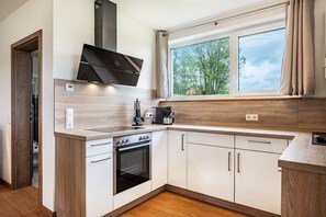 Una cocina moderna con horno empotrado, cafetera y ventana con vista a árboles.
