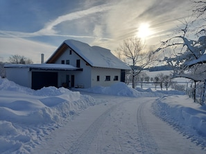 Un paisaje cubierto de nieve con una casa, un camino de entrada y un cielo despejado.