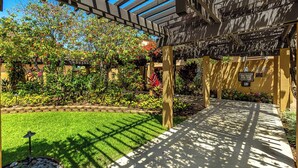 A covered outdoor area with a pathway, greenery, and a pergola structure. - Beachfront condo w/ ocean views and 4 resort pools (Wailea-Makena)