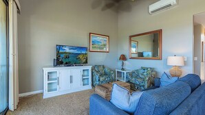 A living room with a sofa, a television, a cabinet, and a mirror. - Beachfront condo w/ ocean views and 4 resort pools (Wailea-Makena)