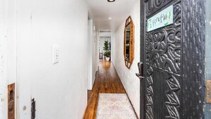 Un couloir avec un plancher en bois, des murs blancs, une porte noire avec une pancarte et, au fond, une plante en pot.