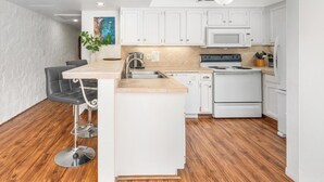 Une cuisine moderne avec des meubles blancs, un évier en acier inoxydable, une cuisinière et un coin bar avec des tabourets.