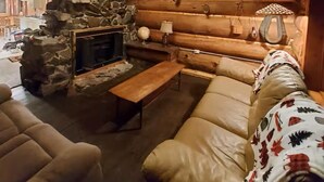 A log cabin interior with a stone fireplace, leather sofa, and wooden beams.