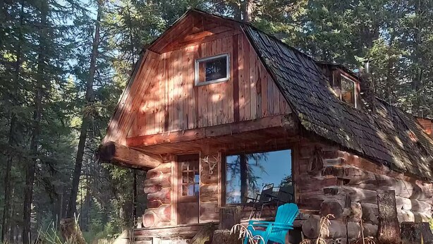 A rustic cabin with a porch, a window, and a chair.