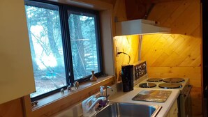 A kitchen with a window, stainless steel sinks, a stove, and wooden cabinetry.