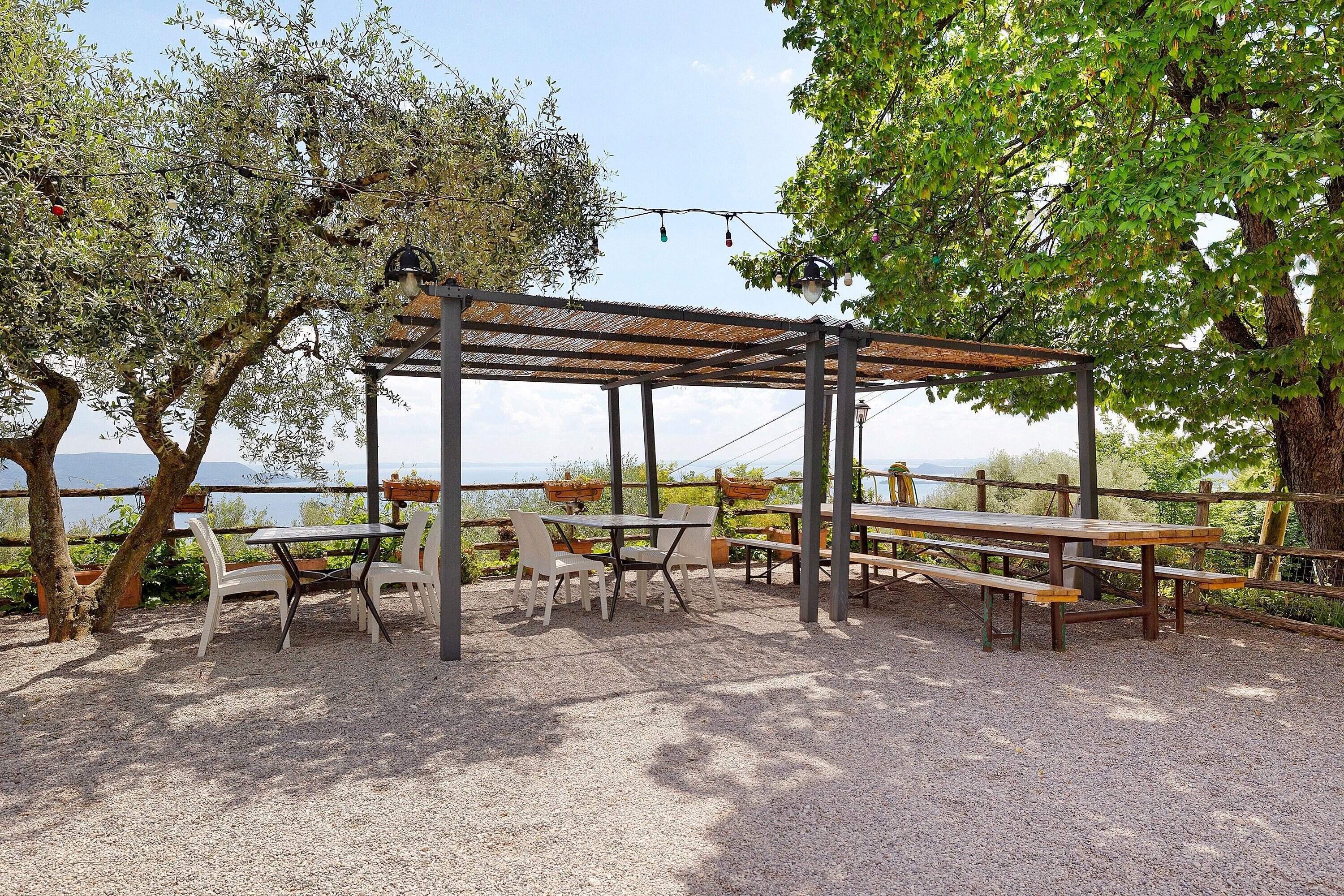 Un espacio al aire libre con mesas, sillas, una pérgola y árboles.