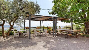 Un espacio al aire libre con mesas, sillas, una pérgola y árboles.
