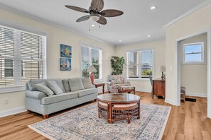 Sink into the plush sofa and enjoy coastal vibes in this bright living room, where natural light and tropical touches create your perfect relaxation space. - Sound Views, Ocean Peeks + 2 Living Areas | Dogs OK | Walk to Beach (Emerald Isle)