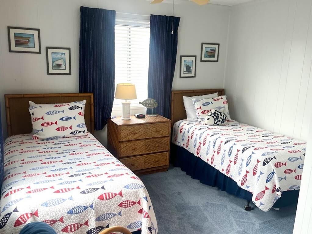 Un dormitorio con dos camas, una mesita de noche, una lámpara y cortinas.