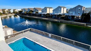 A swimming pool with a fountain, surrounded by a wooden deck and a water canal. - Beachside Condo / Linens Provided! By Williamson Realty (Ocean Isle Beach)