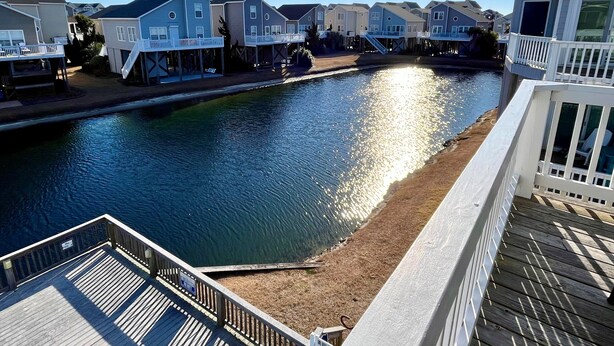 A residential area with houses along a water body, a wooden deck, and a clear sky. - Beachside Condo / Linens Provided! By Williamson Realty (Ocean Isle Beach)