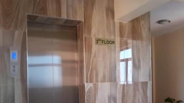 Un ascensor con un letrero que indica '3er Piso', un panel de control y una planta en maceta en un pasillo con suelo de baldosas.