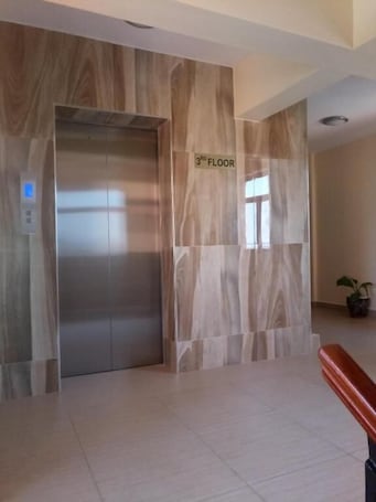 An elevator with a '3rd Floor' sign, a control panel, and a potted plant in a hallway with tiled flooring.
