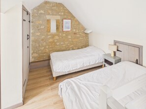 A bedroom with two beds, a wooden floor, a stone wall, a door, and a bedside table with a lamp. - House with pool 50 m from Lascaux IV for two (Montignac)