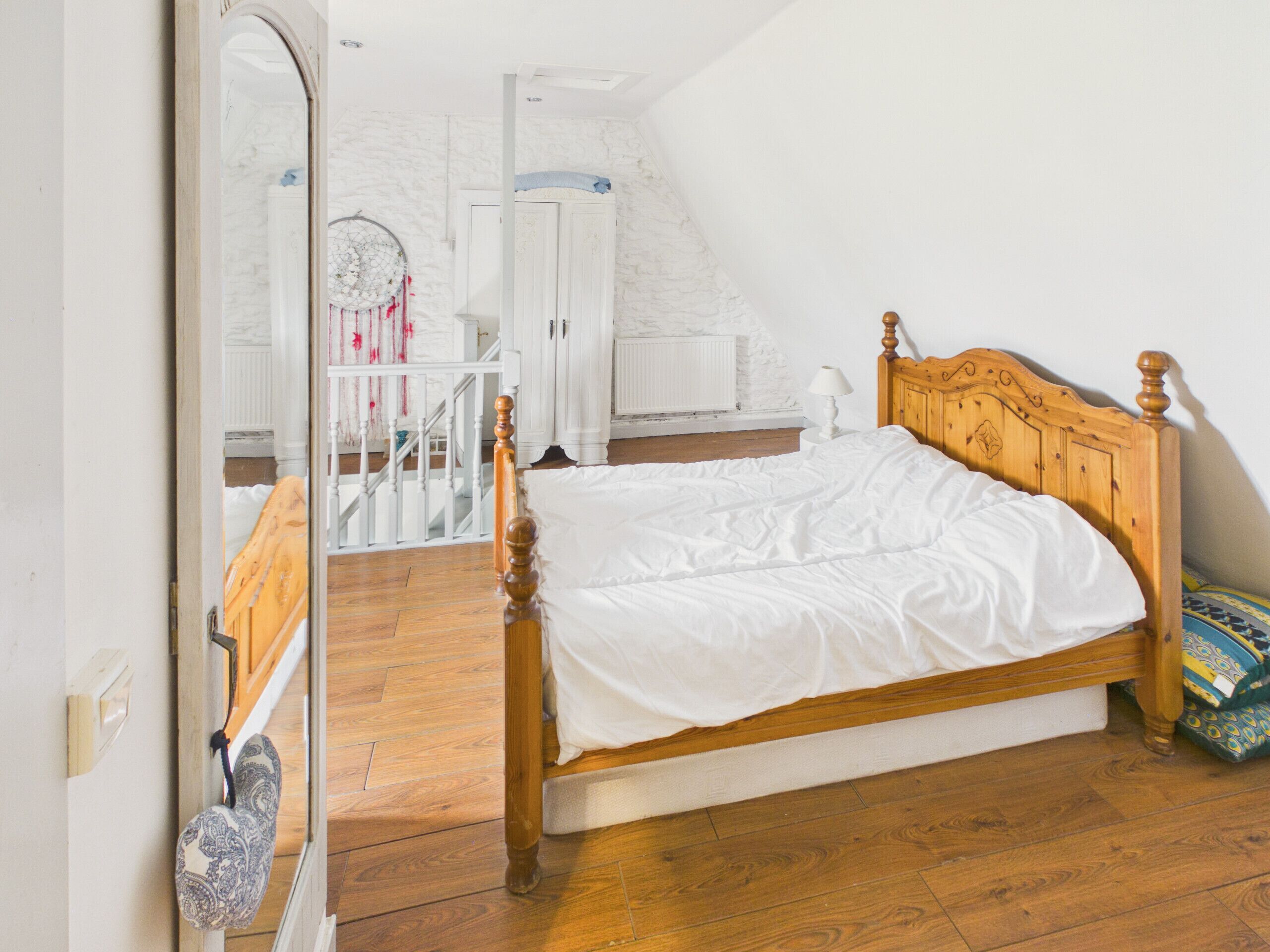 A bedroom with a wooden bed, white walls, a white radiator, and a wooden floor.