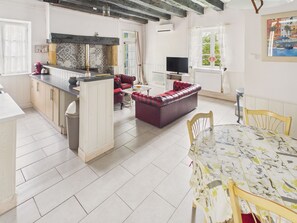 A modern kitchen with a central island, a dining area with a table and chairs, a red sofa, and a television in a living room. - House with pool 50 m from Lascaux IV for 3 (Montignac)